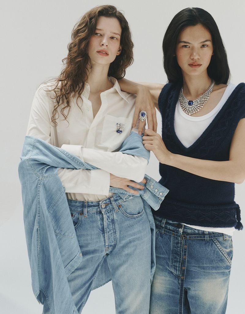 Two female models wearing fine jewellery, denim, and layered casual apparel against a plain white studio backdrop.
