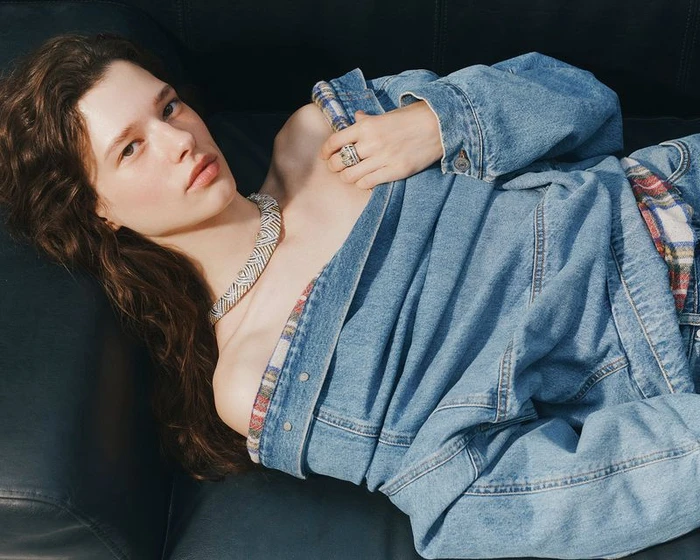 Model wearing a denim jacket and a jeweled statement necklace reclining on a dark couch for Vogue China