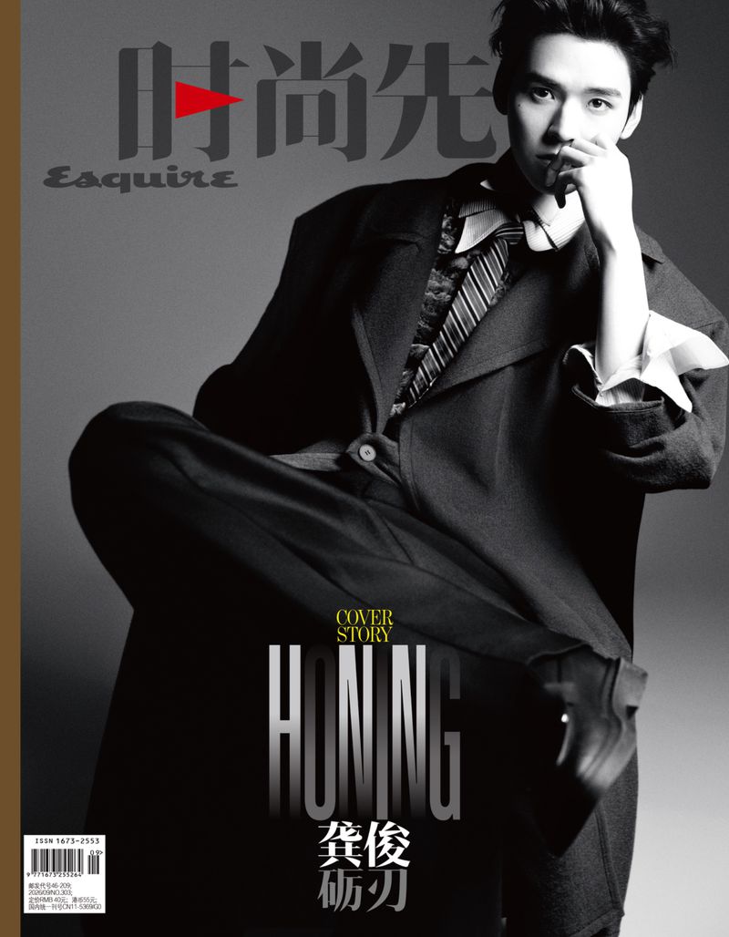 Monochrome fashion editorial portrait of Gong Jun wearing a dark suit jacket and tie against a grey seamless background for Esquire China.