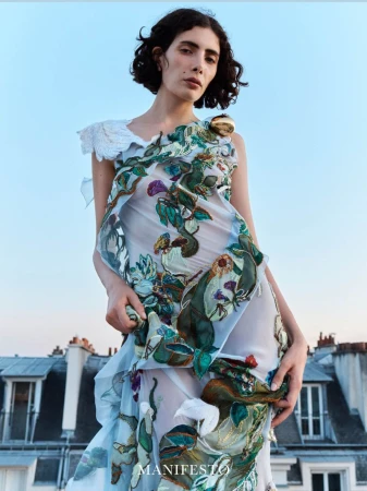 Model wearing an embroidered sheer dress against a rooftop and blue sky background for Manifesto Magazine editorial.