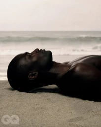 Profile of a shirtless Black man lying on a sandy beach with the ocean in the background for GQ Turkey.