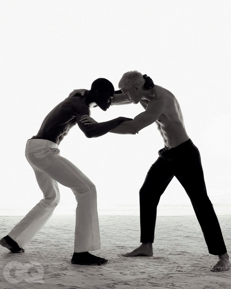 Two shirtless male models grappling in a low-key fashion editorial on sandy terrain for GQ Turkey.