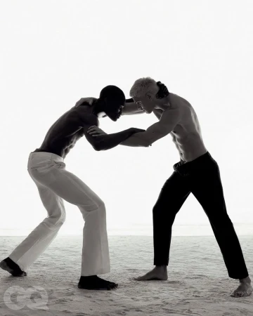 Two shirtless male models grappling in a low-key fashion editorial on sandy terrain for GQ Turkey.