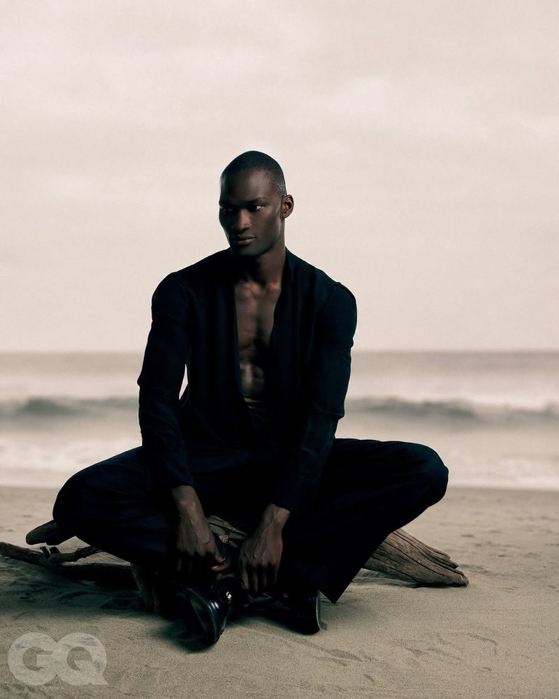 Black man seated on a sandy beach wearing a dark suit jacket and trousers for GQ Turkey