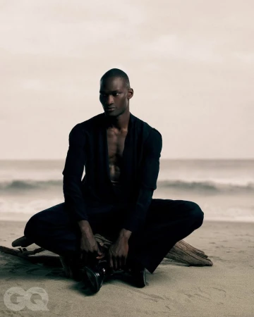 Black man seated on a sandy beach wearing a dark suit jacket and trousers for GQ Turkey