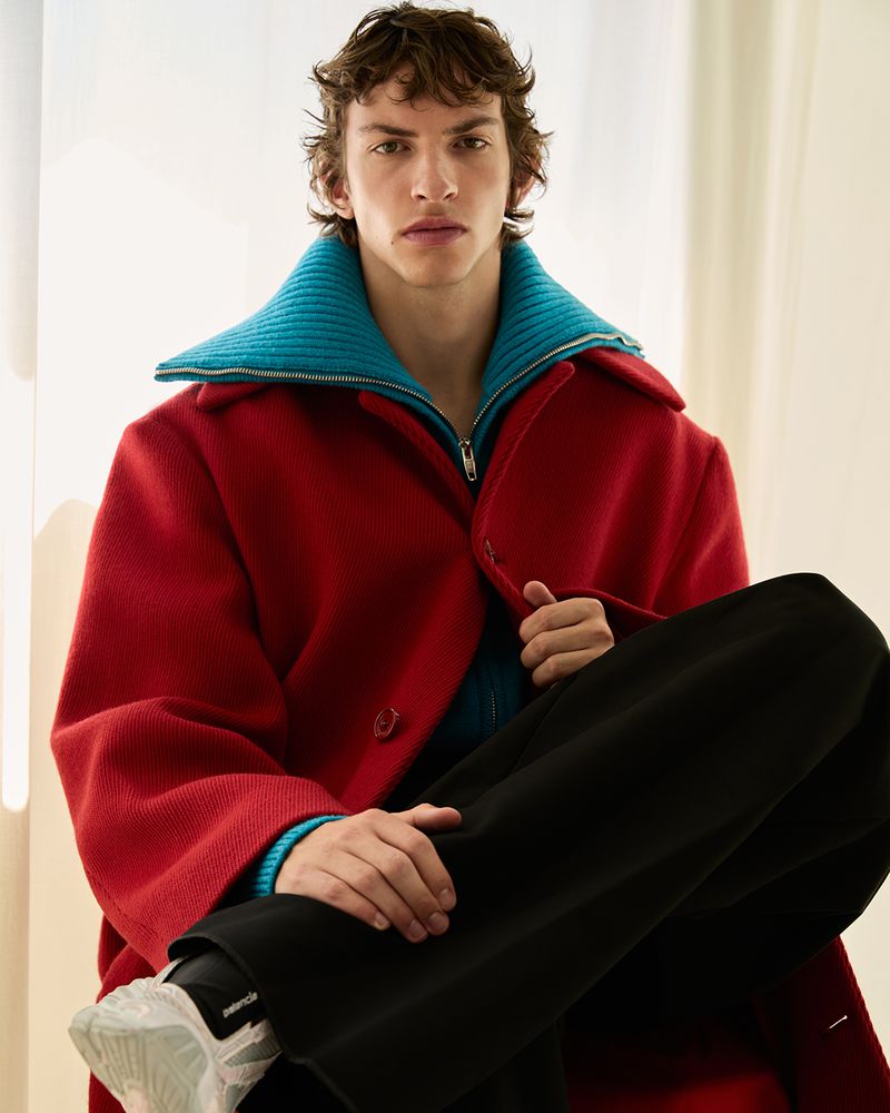 Young male model wearing a red coat with a blue collar and black trousers, photographed by Carlotta Manaigo for Wallpaper China.
