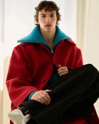 Young male model wearing a red coat with a blue collar and black trousers, photographed by Carlotta Manaigo for Wallpaper China.