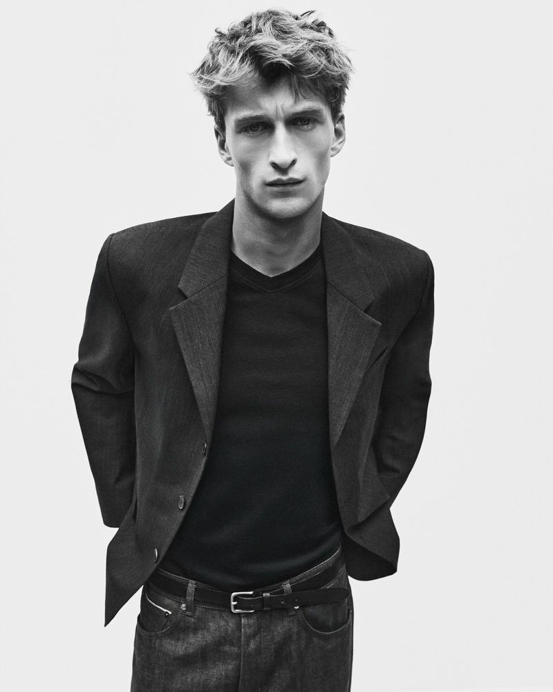 Portrait of a young male model wearing a dark blazer over a t-shirt against a plain studio background.