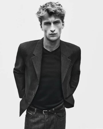 Portrait of a young male model wearing a dark blazer over a t-shirt against a plain studio background.