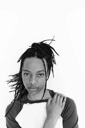 Portrait of a Black model with locs wearing a two-tone raglan top against a seamless white background for H&M.