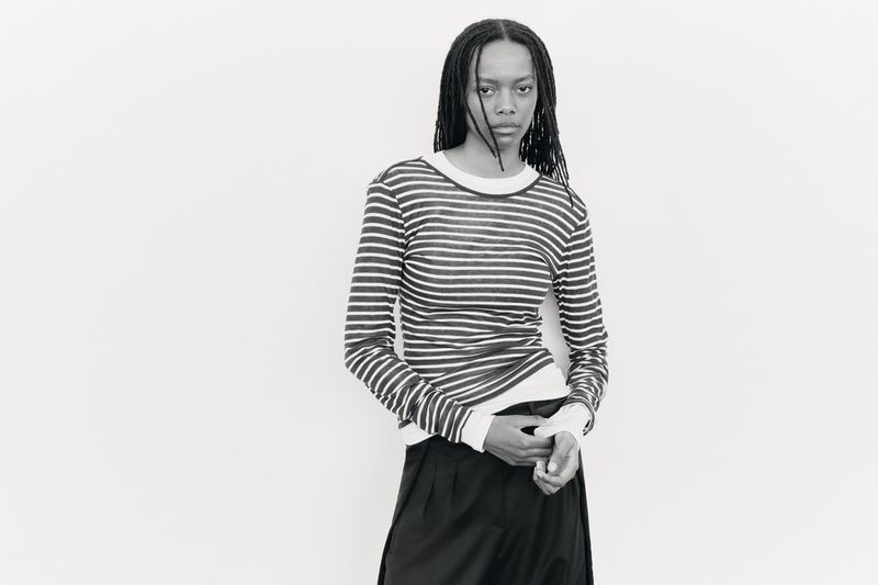 Model with long dark dreadlocks wearing a striped long-sleeve top against a plain light background