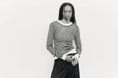 Model with long dark dreadlocks wearing a striped long-sleeve top against a plain light background