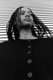 Model with locs wearing a black buttoned cardigan against a textured metal wall for H&M Clean Lines project.