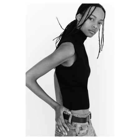 Model Nyela Hopster wearing a black mock neck top and denim jeans against a white seamless backdrop