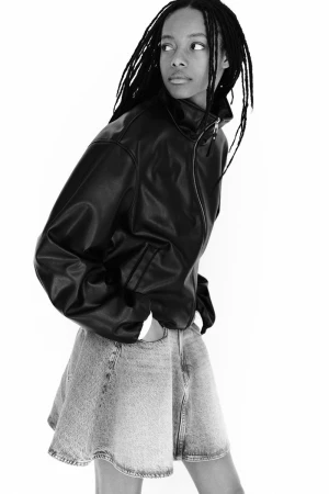 Model wearing a black leather jacket and denim skirt against a white studio background for H&M Clean Lines project
