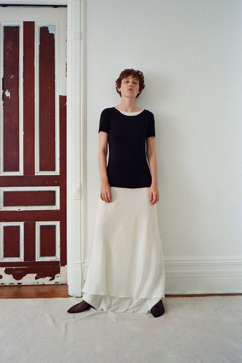 Model Annabelle Weatherly wearing a black top and white skirt standing against a white wall by a red door