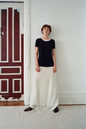 Model Annabelle Weatherly wearing a black top and white skirt standing against a white wall by a red door