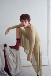 Model Annabelle Weatherly in a long sheer beige outfit with dark red socks posing in a white interior for Mel Usine S/S 27