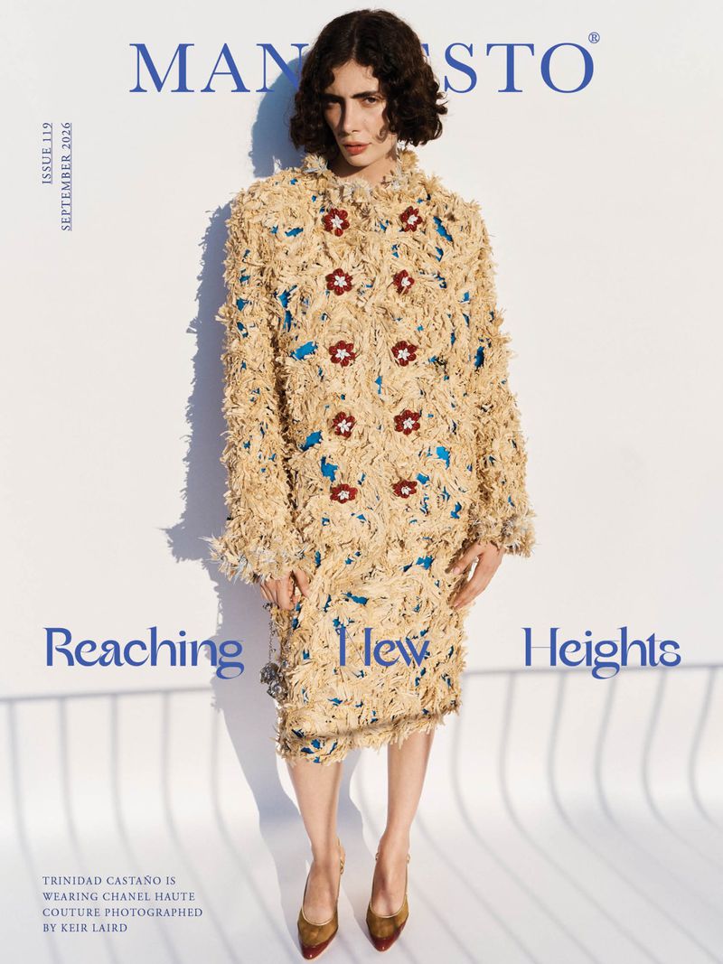 Model Trinidad Castaño wearing textured beige coat with red floral embellishments against white background
