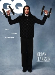 Jordan Clarkson holding dumbbells wearing a black patterned jacket and trousers against a textured grey studio backdrop