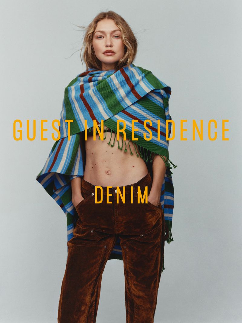 Gigi Hadid wearing a striped green scarf and brown trousers against a grey seamless background for Guest In Residence Denim campaign.