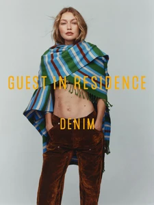 Gigi Hadid wearing a striped green scarf and brown trousers against a grey seamless background for Guest In Residence Denim campaign.