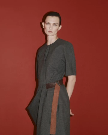 Model Lara Mullen wearing a grey dress with a brown belt against a red background for Bottega Veneta