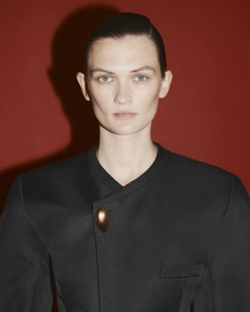 Model Lara Mullen in a black jacket with a gold clasp against a dark red backdrop, photographed by Ferry van der Nat.