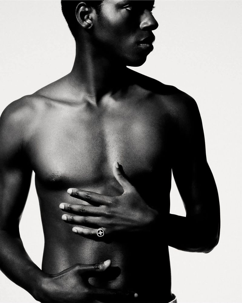 Portrait of a shirtless black male model wearing a ring, shot against a plain white background for Pascale Monvoisin.