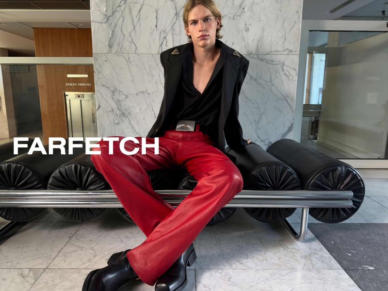 Model seated on a black leather bench wearing a black blazer and red trousers for the Farfetch AW26 campaign.