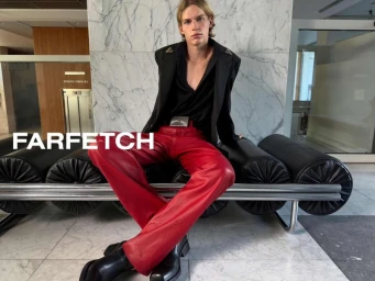 Model seated on a black leather bench wearing a black blazer and red trousers for the Farfetch AW26 campaign.