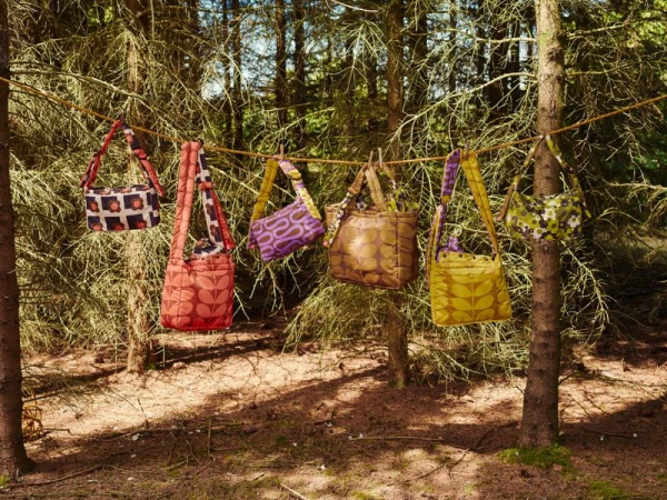 Several patterned canvas handbags hanging from a rope line strung between trees in a forest setting.
