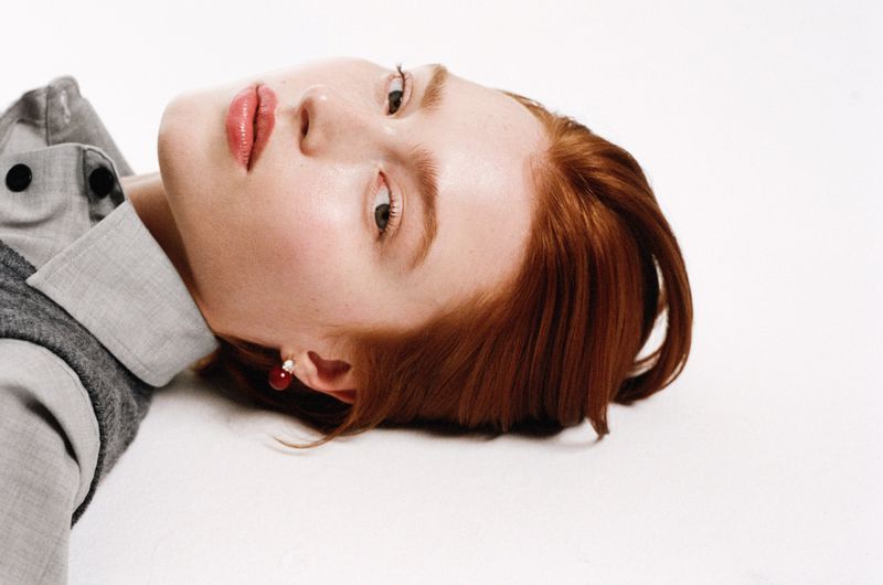 Model with red hair wearing a grey collared shirt against a white background