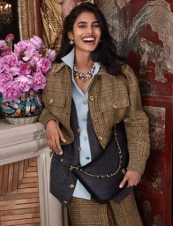 South Asian model smiling in a textured tweed jacket and holding a black quilted handbag indoors