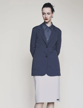 Model wearing a dark blazer and light skirt standing against a neutral background for Harper's Bazaar Germany.