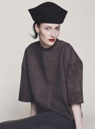 Model wearing a structured black cap and dark brown top against a neutral off-white background