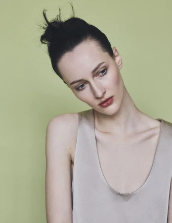 Model with dark hair in a high bun wearing a grey top against a muted green studio backdrop for Harper's Bazaar Germany
