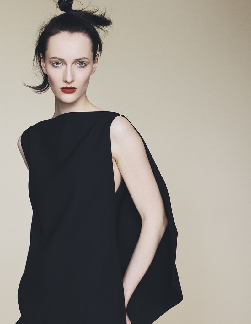 Model wearing a black sleeveless dress with bold red lipstick against a neutral backdrop for Harper's Bazaar Germany