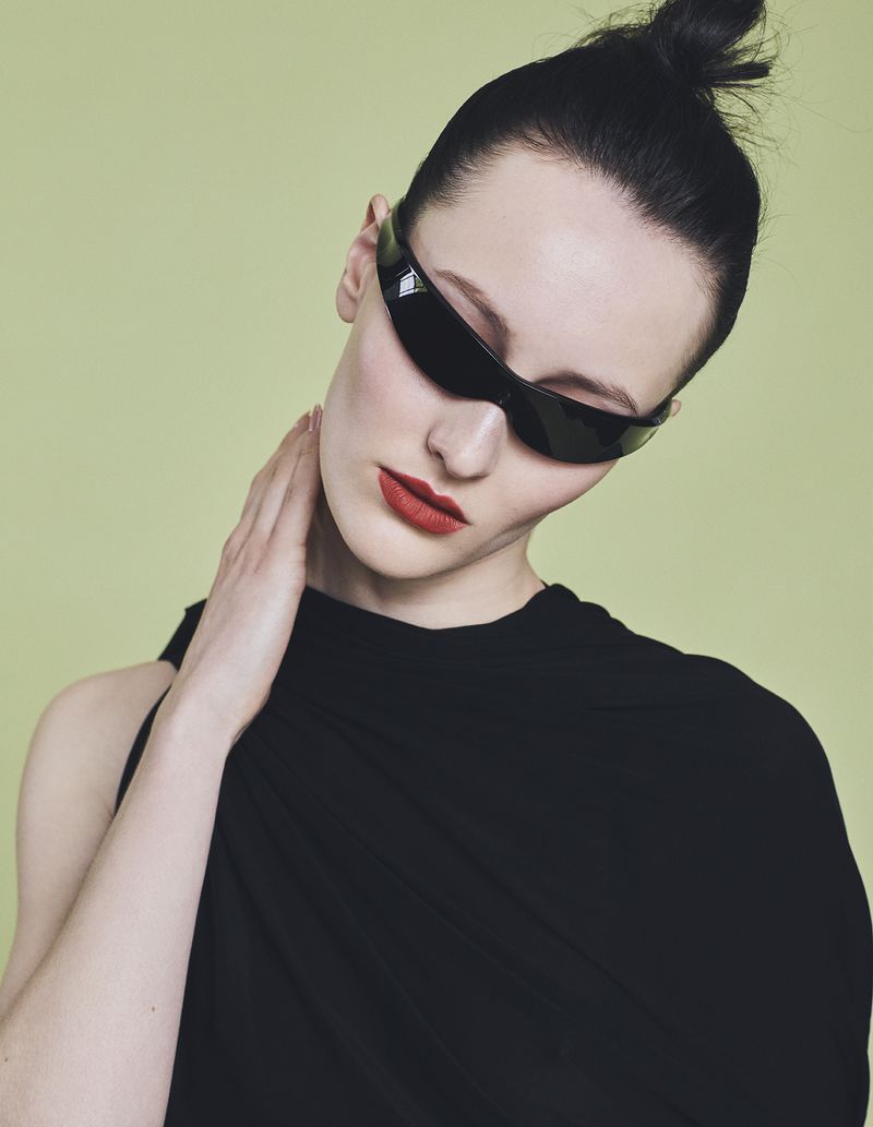 Model wearing dark wrap-around sunglasses and a black top against a pale green background for Harper's Bazaar Germany.