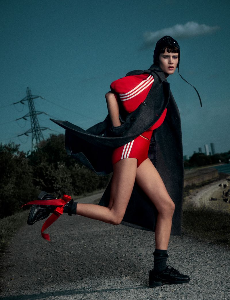 Model Noor Khan wearing a red athletic suit and dark coat running along an outdoor path for AnOther Magazine by Simone Rocha.
