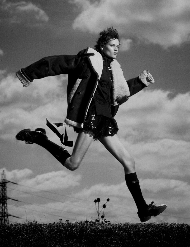 Model in shearling jacket jumping outdoors against a cloudy sky