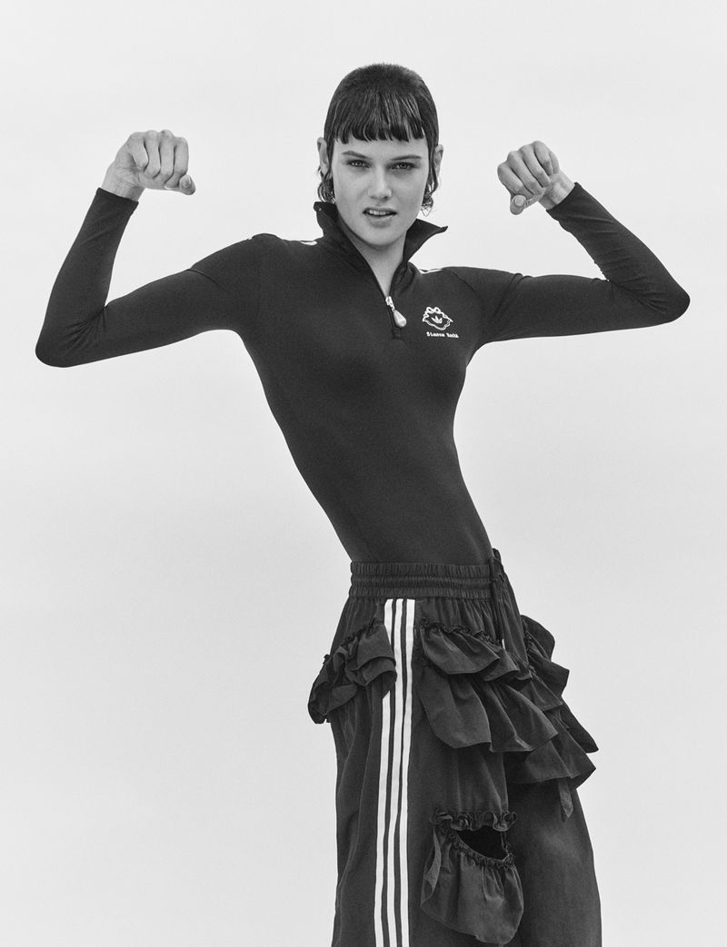 Model in black zipped top and striped ruffled trousers posing against white background for AnOther Magazine by Charlotte Wales