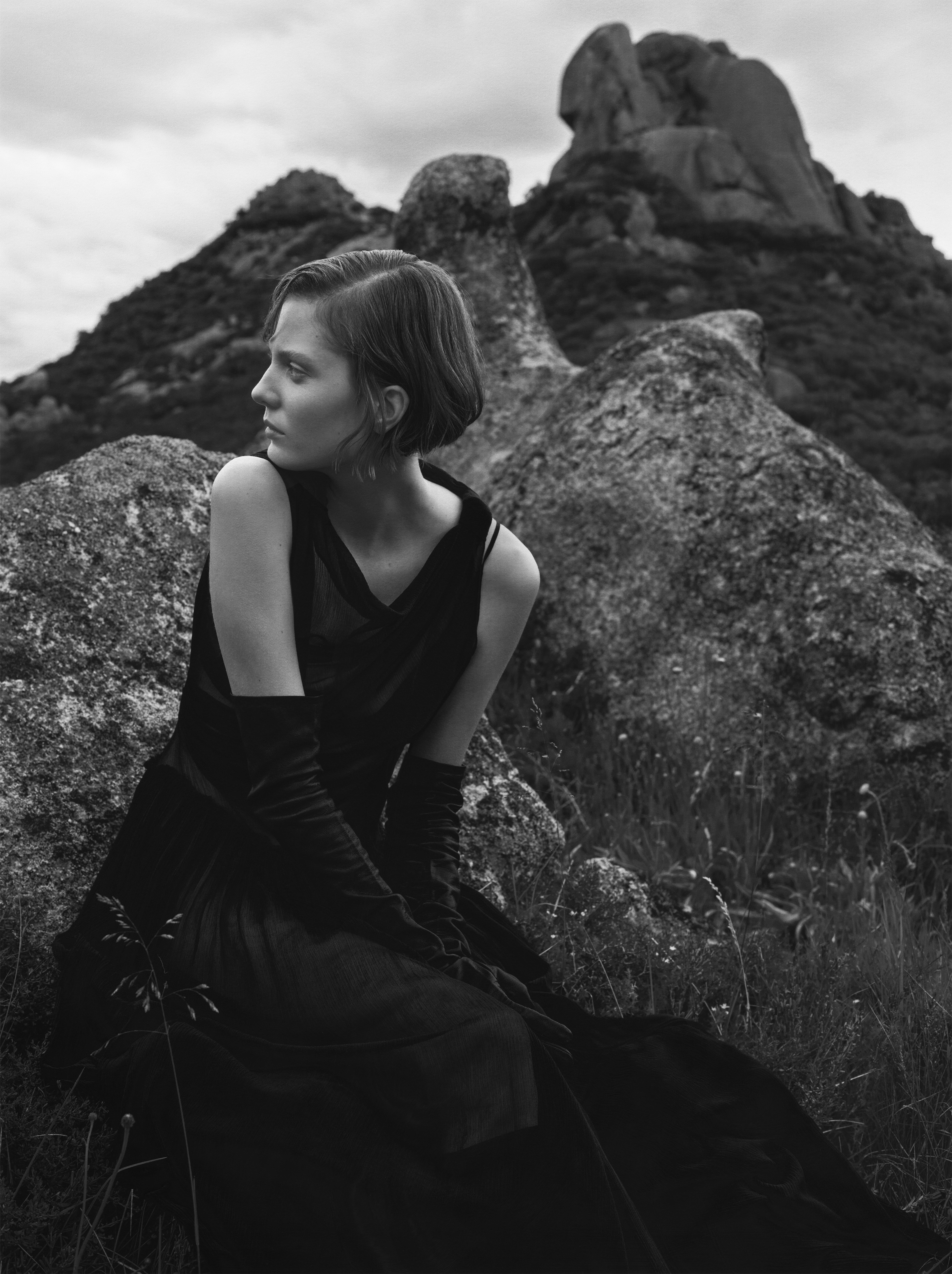 Model wearing dark dress and gloves seated amidst rocky terrain for Vogue Polska High Country editorial