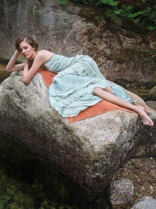 Woman in pale green strapless dress reclining on a large wet rock over a stream for Vogue Polska by James Giles.