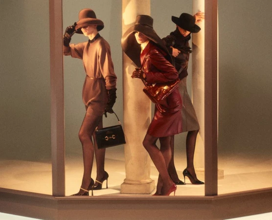 Three models wearing wide-brimmed hats and holding handbags pose between architectural columns in an editorial fashion shoot.