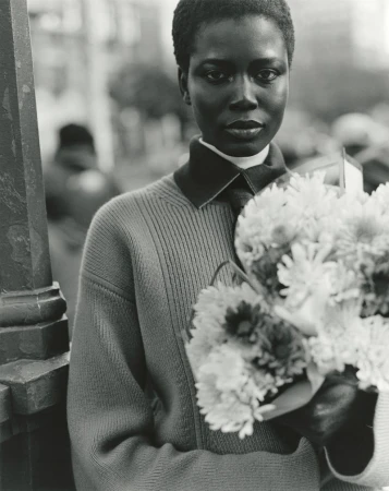 Black model holding a large bouquet of flowers wearing a collared sweater on a city street in a black and white fashion portrait.