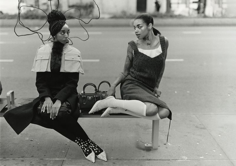 Two black female models sitting on a city bench outdoors for a fashion editorial for 10 Magazine