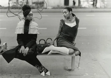 Two black female models sitting on a city bench outdoors for a fashion editorial for 10 Magazine
