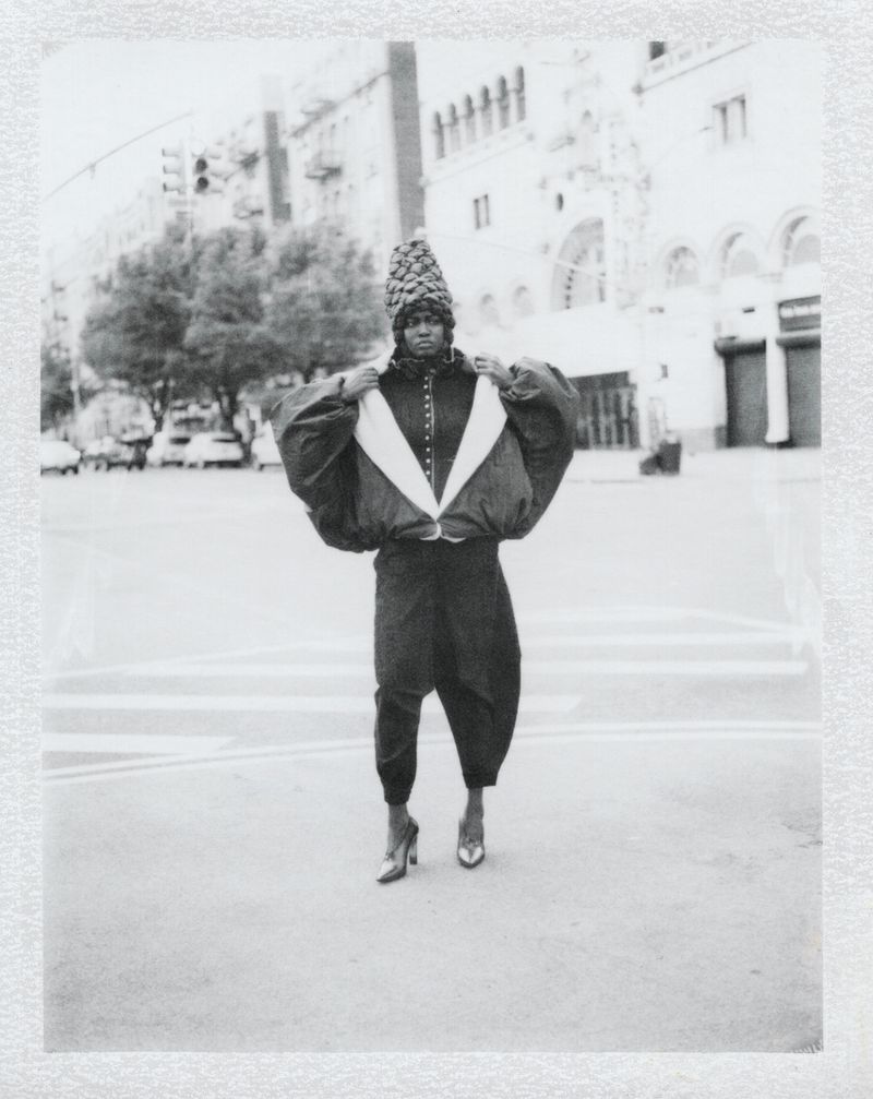 Black and white editorial portrait of a model in avant-garde clothing posing on an urban street.