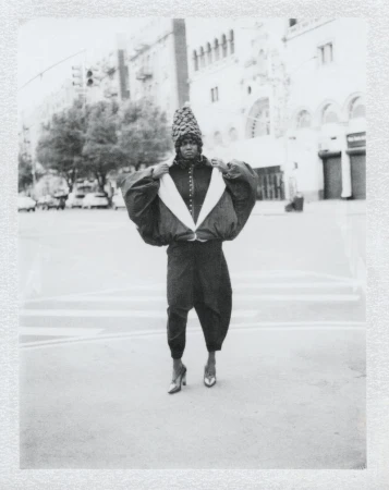 Black and white editorial portrait of a model in avant-garde clothing posing on an urban street.